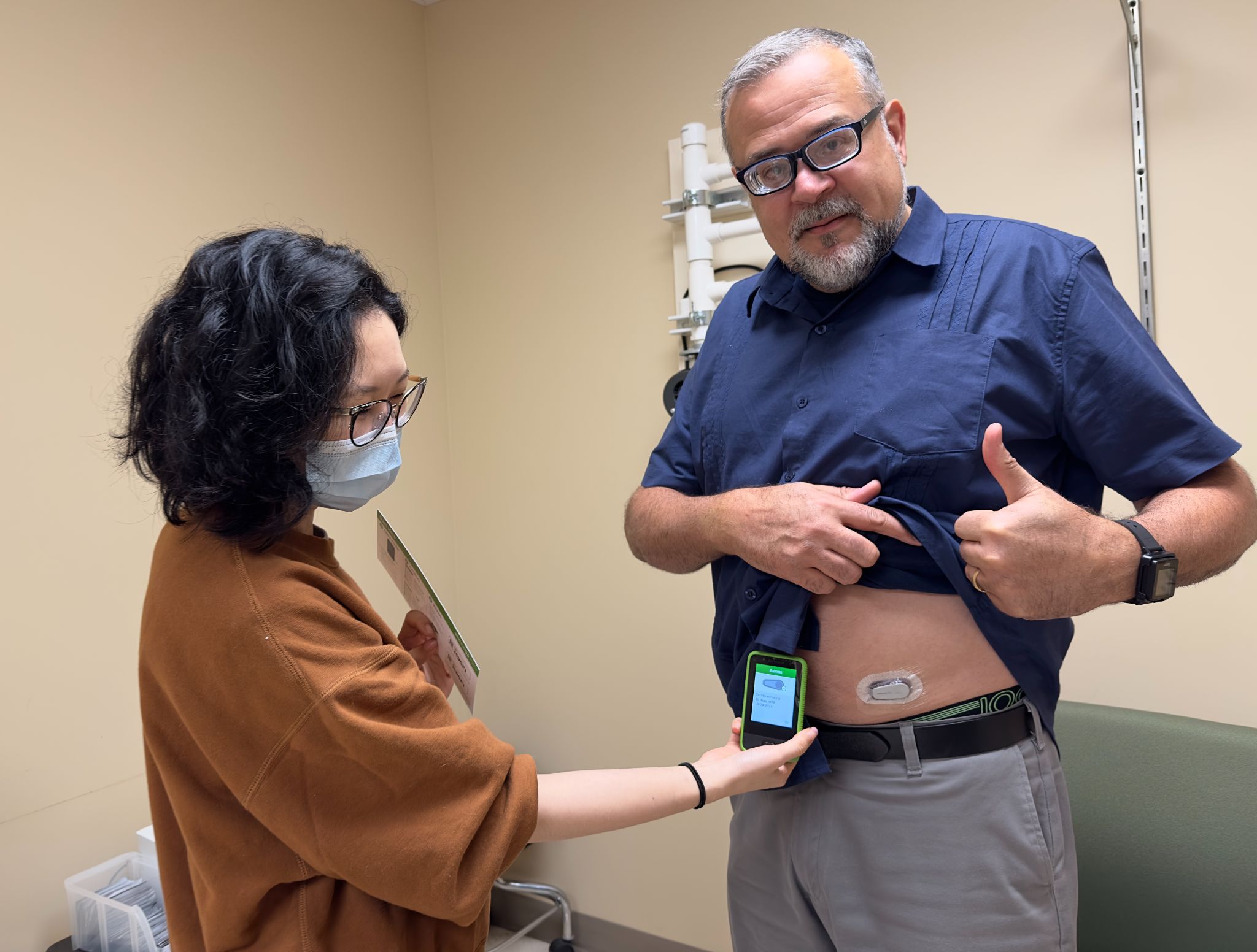 Elaine Wang, clinical research coordinator for the UC Davis-WHRNC Nutrition for Precision Health study, checks the continuous blood glucose monitor Hugo Campos received as part of the study. Photo credit: UC Davis Health